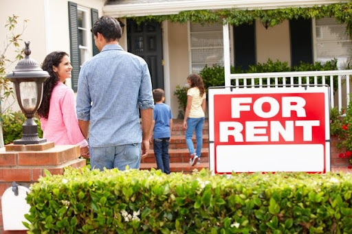 A family standing in front of a house with a "For Rent" sign, with children walking towards the door.