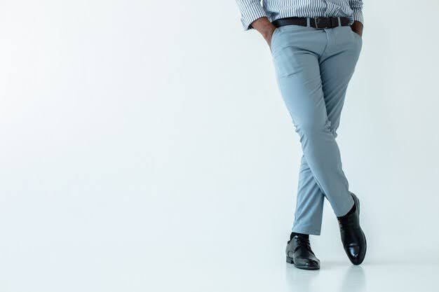 Man wearing light blue formal trousers and black dress shoes, standing with crossed legs against a clean white background.