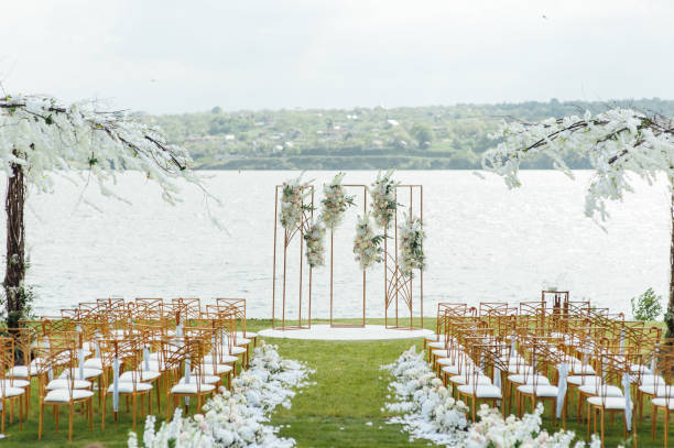 Outdoor lakeside wedding ceremony setup with a floral arch, white chairs, and green aisle by the water.