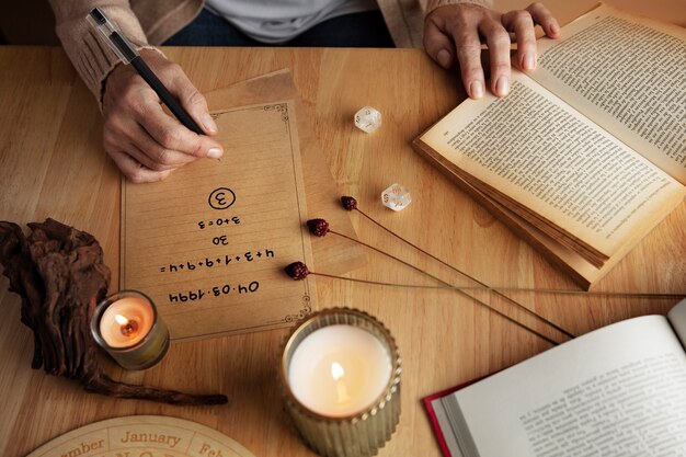 A person writes numbers on parchment at a wooden table with candles, crystals, incense, and an open book nearby.