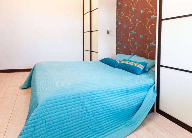 Minimalist bedroom with turquoise bedspread, decorative floral wall panel, and sliding shoji-style doors.